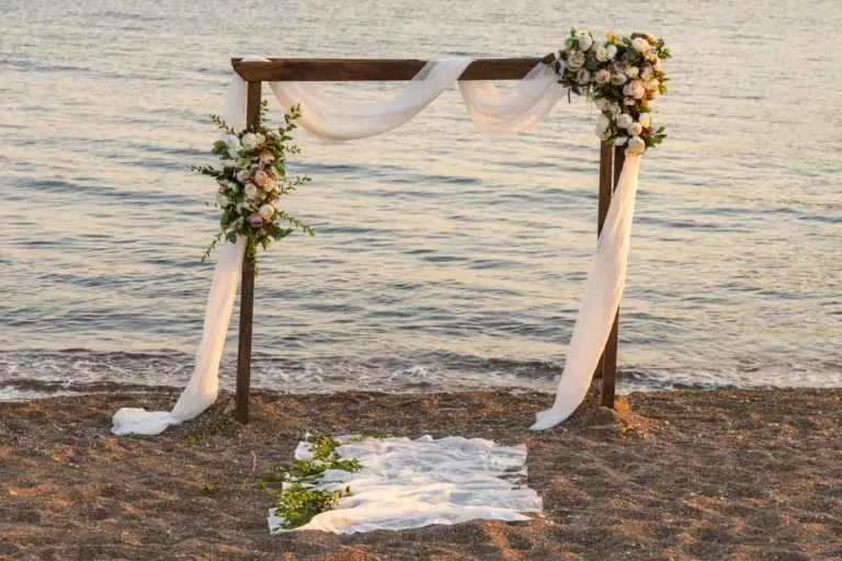 Arco de boda decorado con flores y telas blancas en la orilla de la playa
