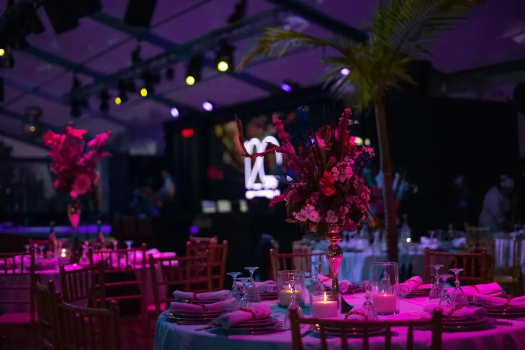 Carpa de evento iluminada en fucsia con mesas montadas y centros florales altos