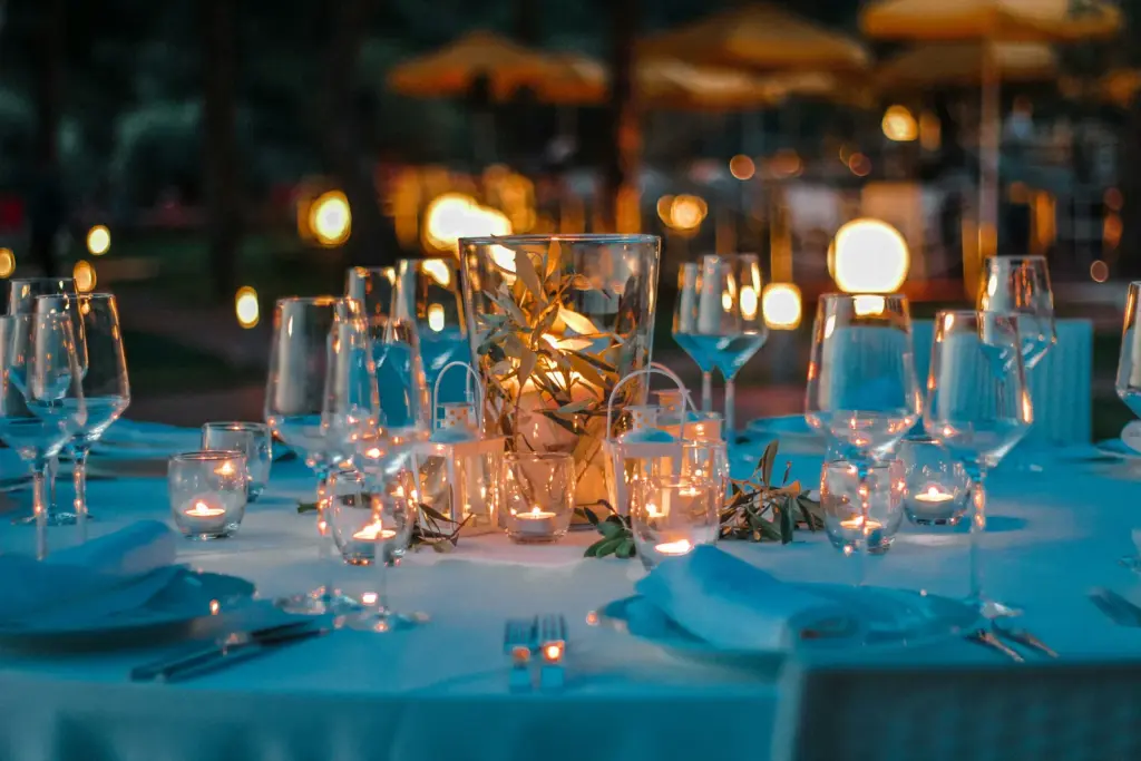 Mesa de cena al aire libre con velas, cristalería y ramas de olivo al anochecer