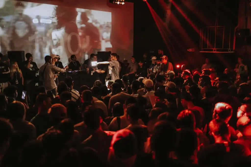 Público en una sala durante un directo, con la cabina de DJ al fondo